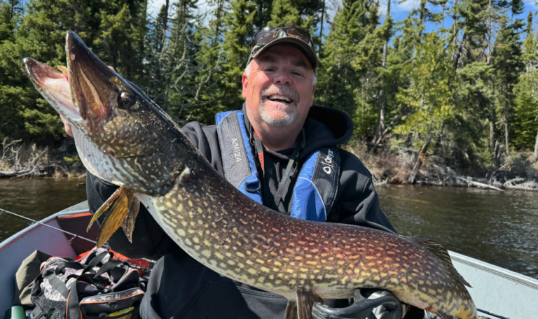 Jim holding a large fish while fishing at a lake on a clear day.